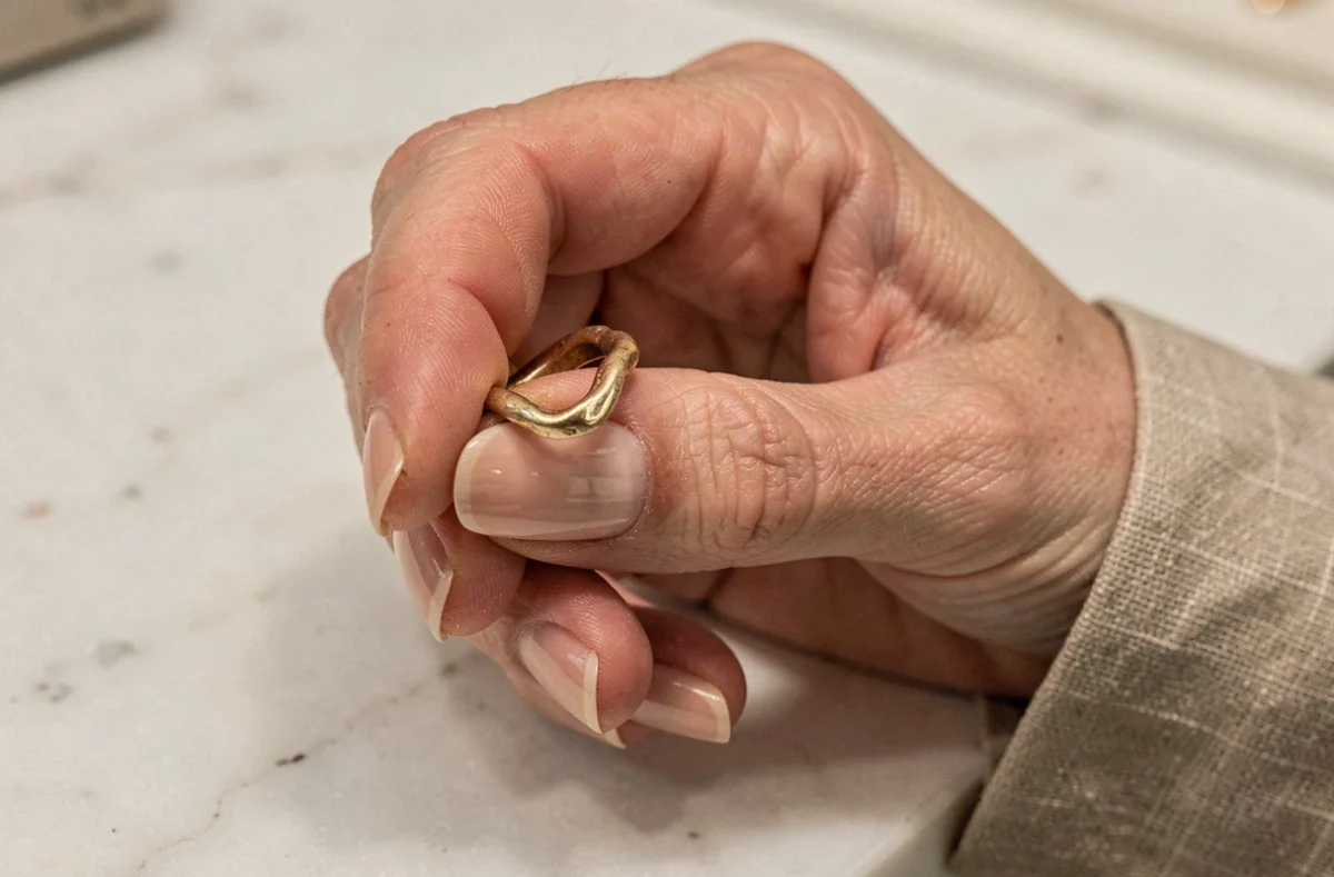 Main de femme tenant une vieille bague en or déformée au-dessus d'un comptoir en marbre dans une bijouterie