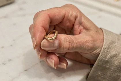 Main de femme tenant une vieille bague en or déformée au-dessus d'un comptoir en marbre dans une bijouterie