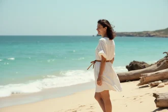 Femme portant une robe chemise blanche ceinturée sur une plage méditerranéenne, silhouette légère et taille sculptée
